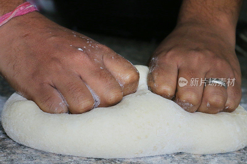 一个男人揉面团做面包卷/披萨/面包条的形象，在家庭厨房里的家庭烘焙，在花岗岩厨房工作台上用老式的手工揉面